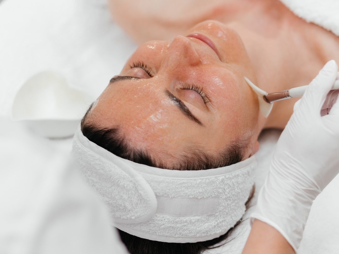 Frau mit geschlossenen Augen erhält eine Gesichtsanwendung in einem Spa.