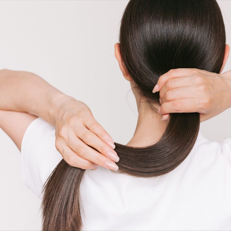 Eine Person bindet ihre langen, glatten Haare zu einem Pferdeschwanz.